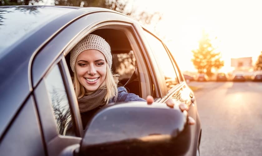 Женщина смотрит в автомобильное зеркало, чтобыa избежать повреждений автомобиля.